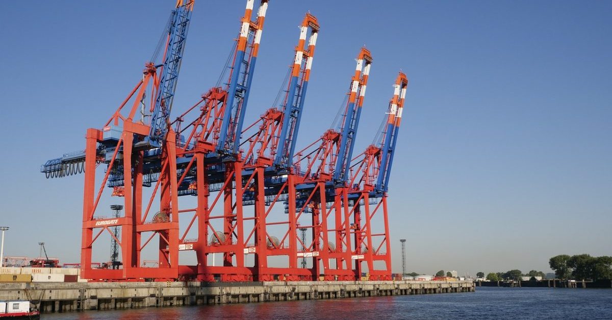 Large cargo cranes at a port by the water.