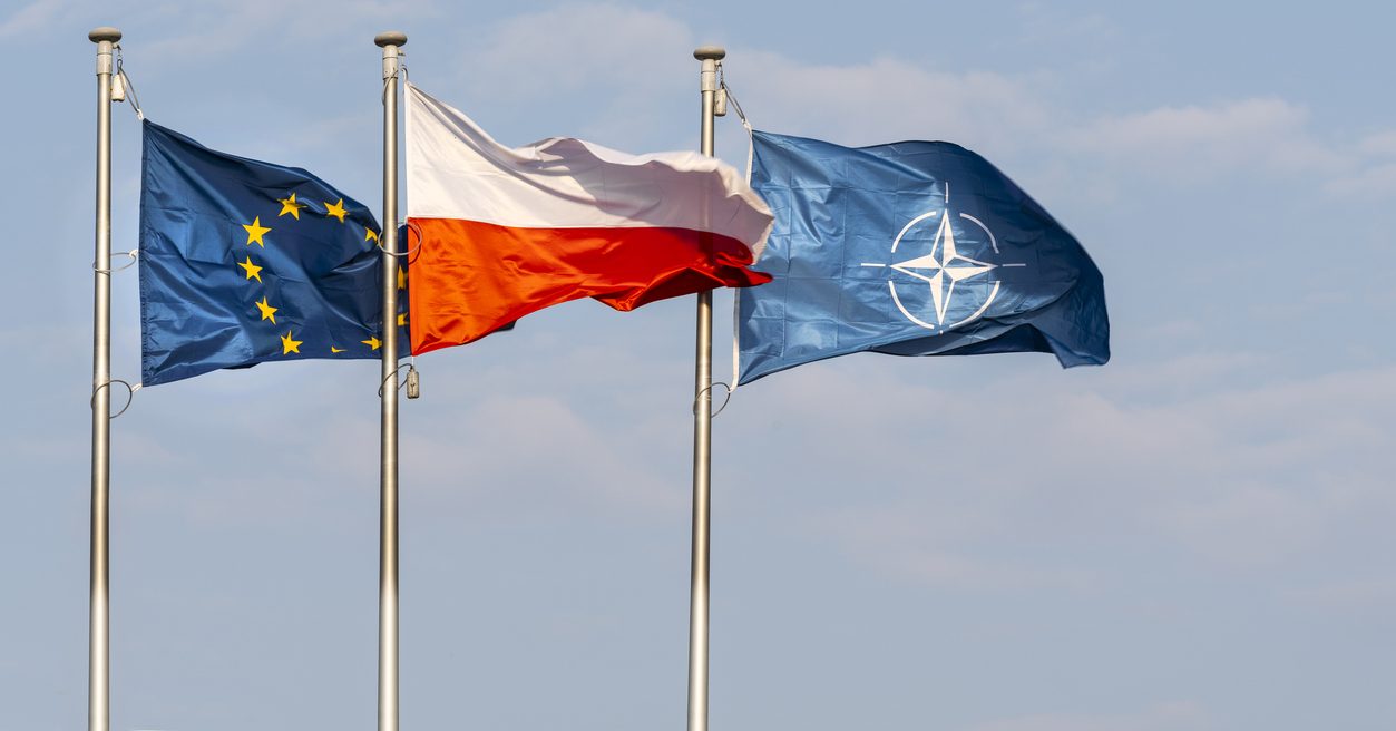 The flags of Poland, Europe and NATO waving on a blue sky