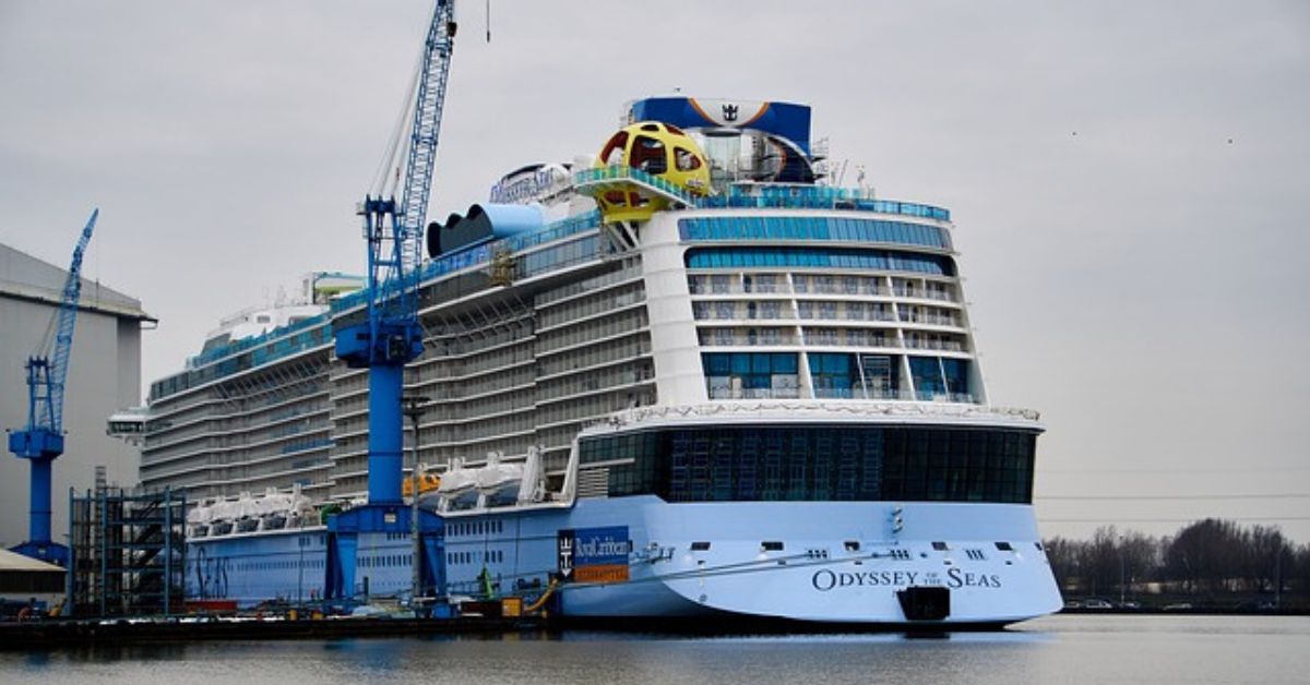 Large cruise ship docked at a shipyard with cranes.