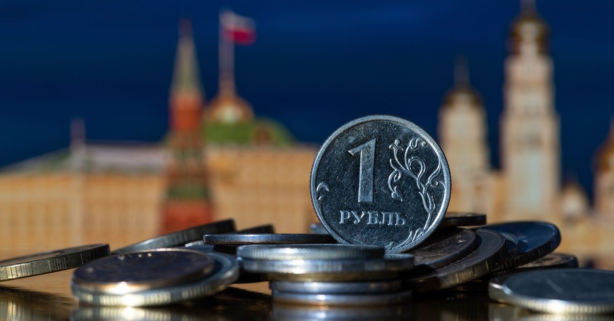 Russian ruble coin in front of a blurred Kremlin background.