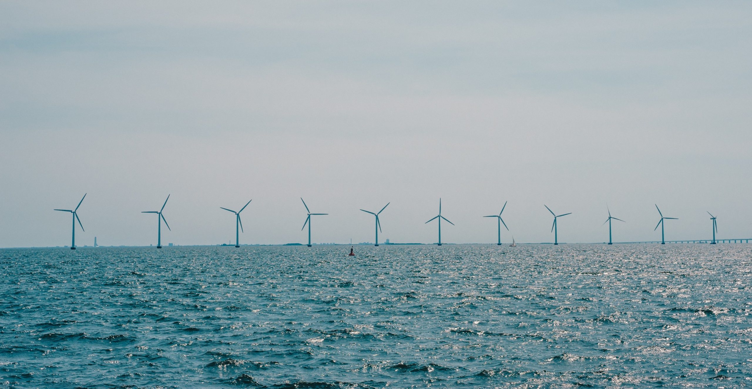 Offshore wind turbines lined up across the Baltic sea horizon under a hazy sky.