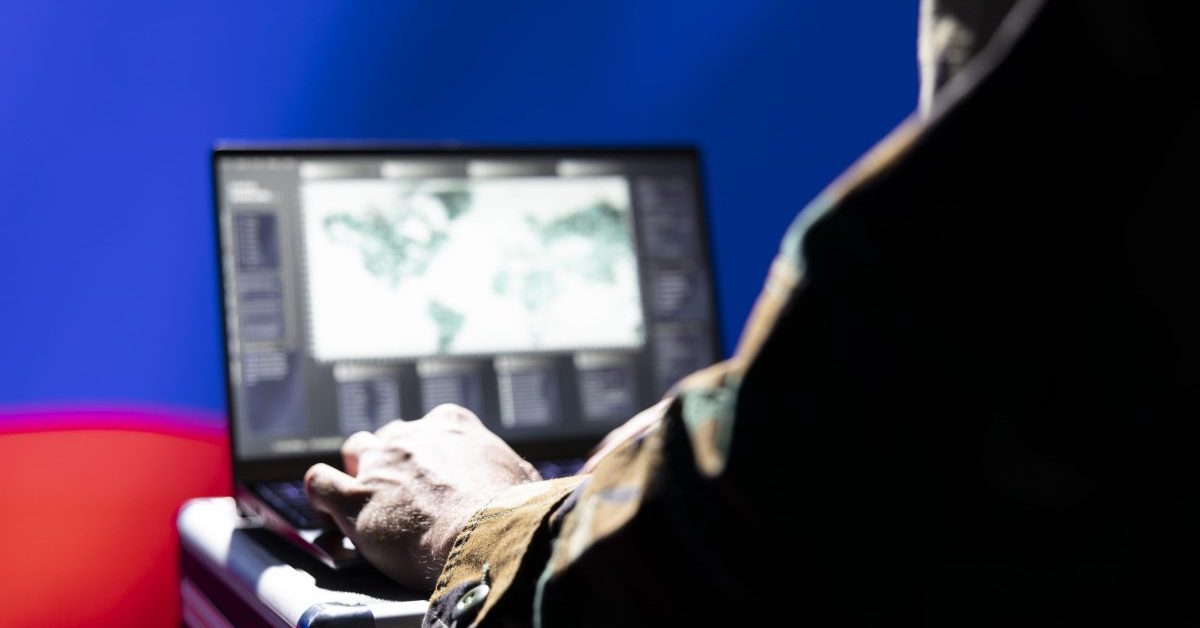 Russian flag on the background and person using a laptop with a map interface, suggesting cyber or intelligence activity.