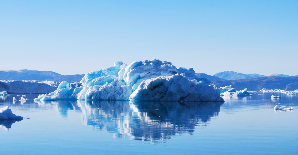 An iceberg floating in the sea, with its reflection visible on the water's surface.