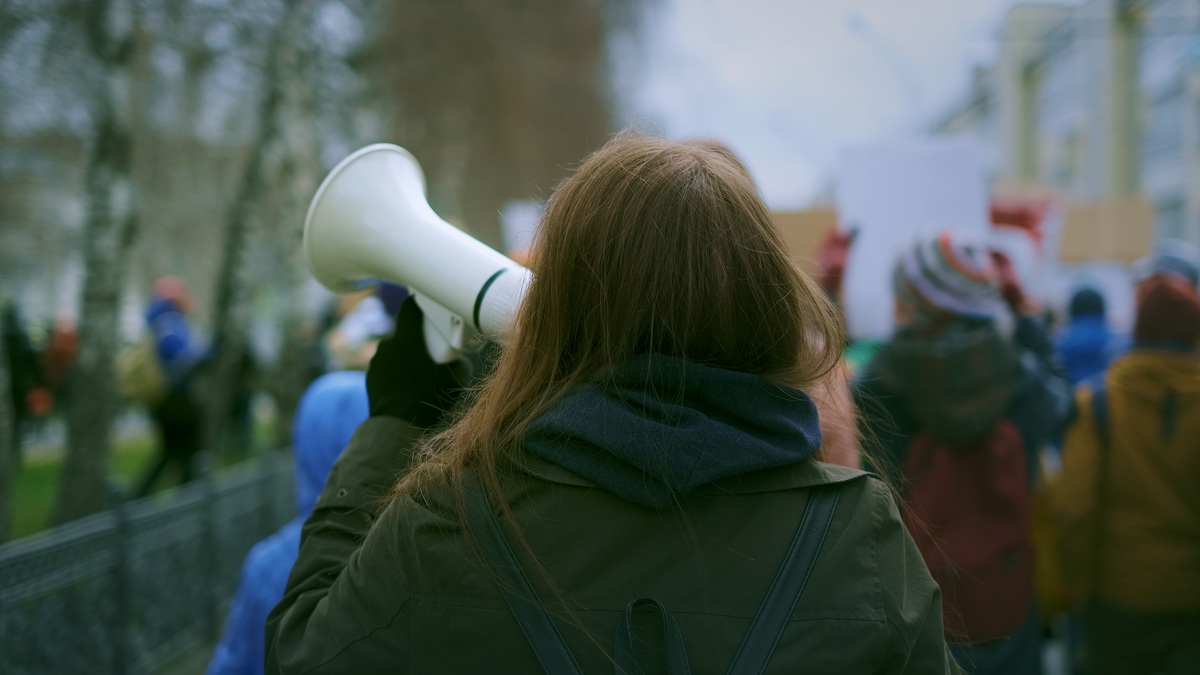 Takaapäin kuvattu nainen puhuu megafoniin mielenosoituksessa