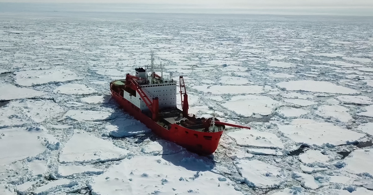 A red-and-white icebreaker is opening a navigation channel in the middle of big ice floats.