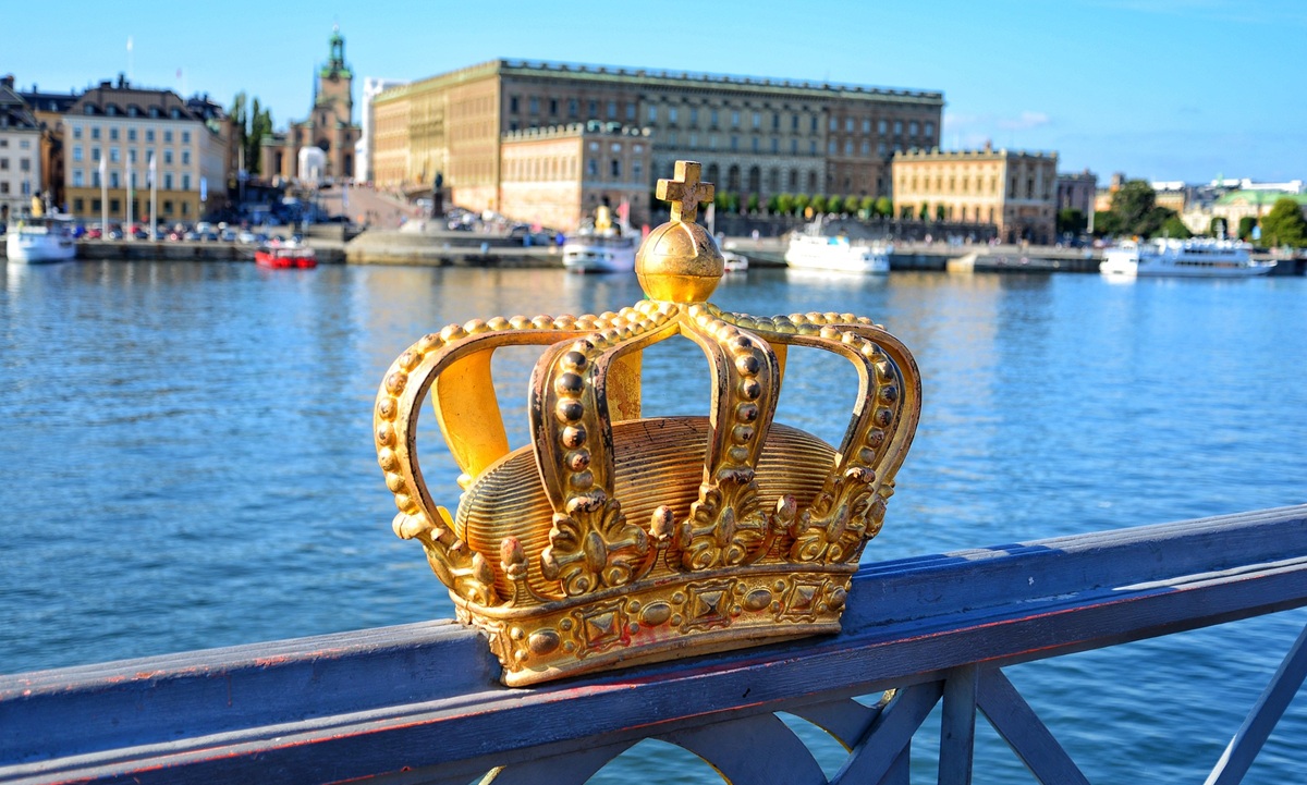 Näkymä Tukholman Kuninkaansillalta. Etualalla on sillan kruunukoriste, taustalla on vesistö, kuninkaanlinna ja pieniä matkustaja-aluksia auringonpaisteessa.