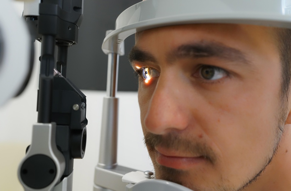 A man undergoes an eye examination using a slit-lamp microscope, with a bright light illuminating his eye.
