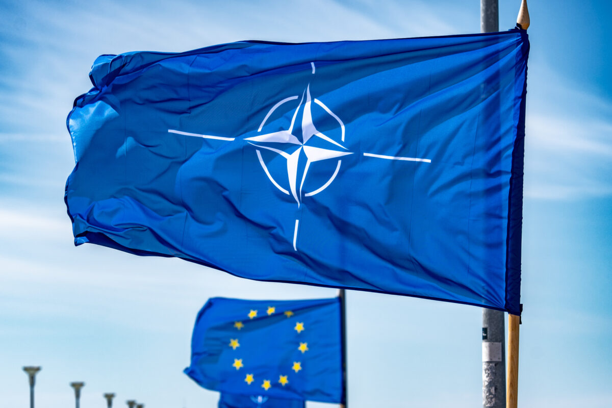 NATO flag waiving on a flagpole with European Union flag behind.