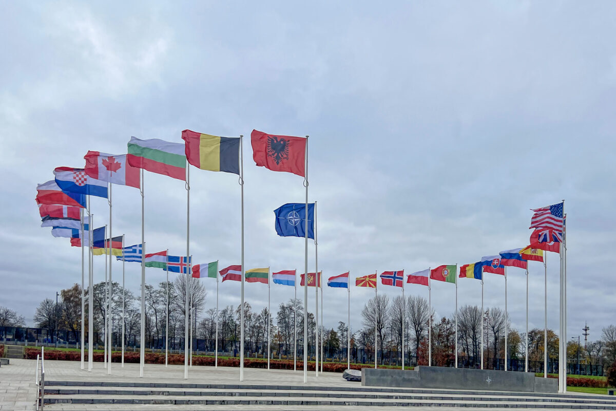 Image of the exterior of NATO Headquarters with the flags of member countries waving in the wind.