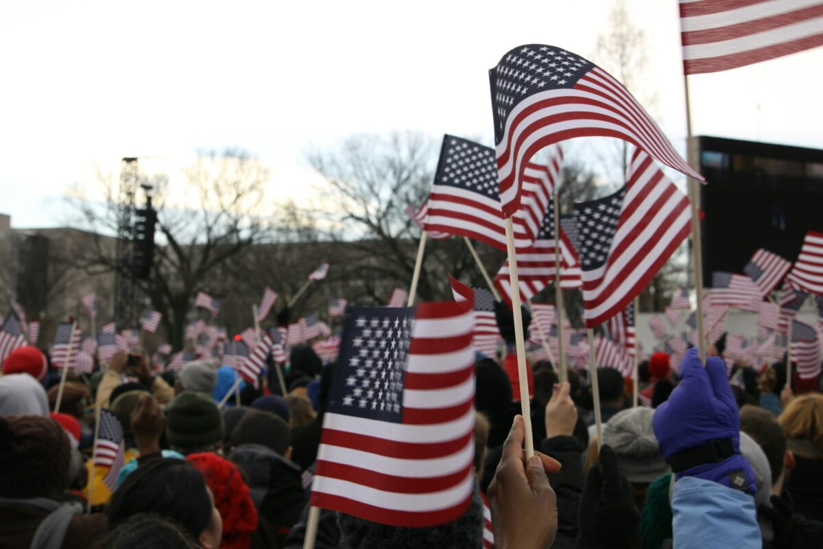 People waving USA flags in the crowd picturing American patriotism and nationalist ideology.